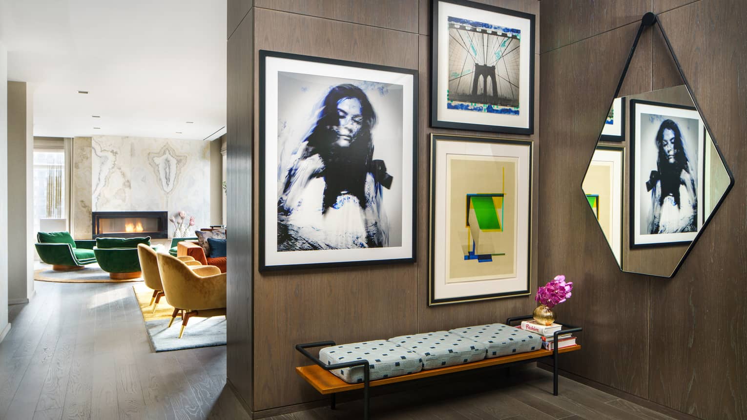Empire suite entryway with wall-mounted modern art, geometric mirror, cushioned bench, and view into a lounge with green and yellow armchairs by a fireplace