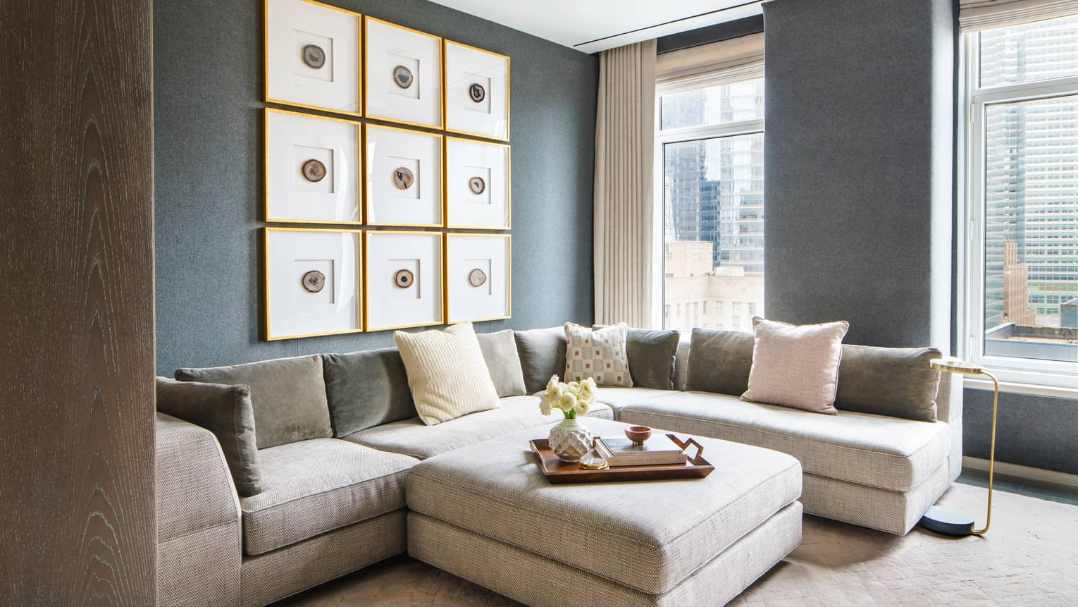 Light grey l-shaped sofa and matching square ottoman set against a slate-blue wall with hanging pictures
