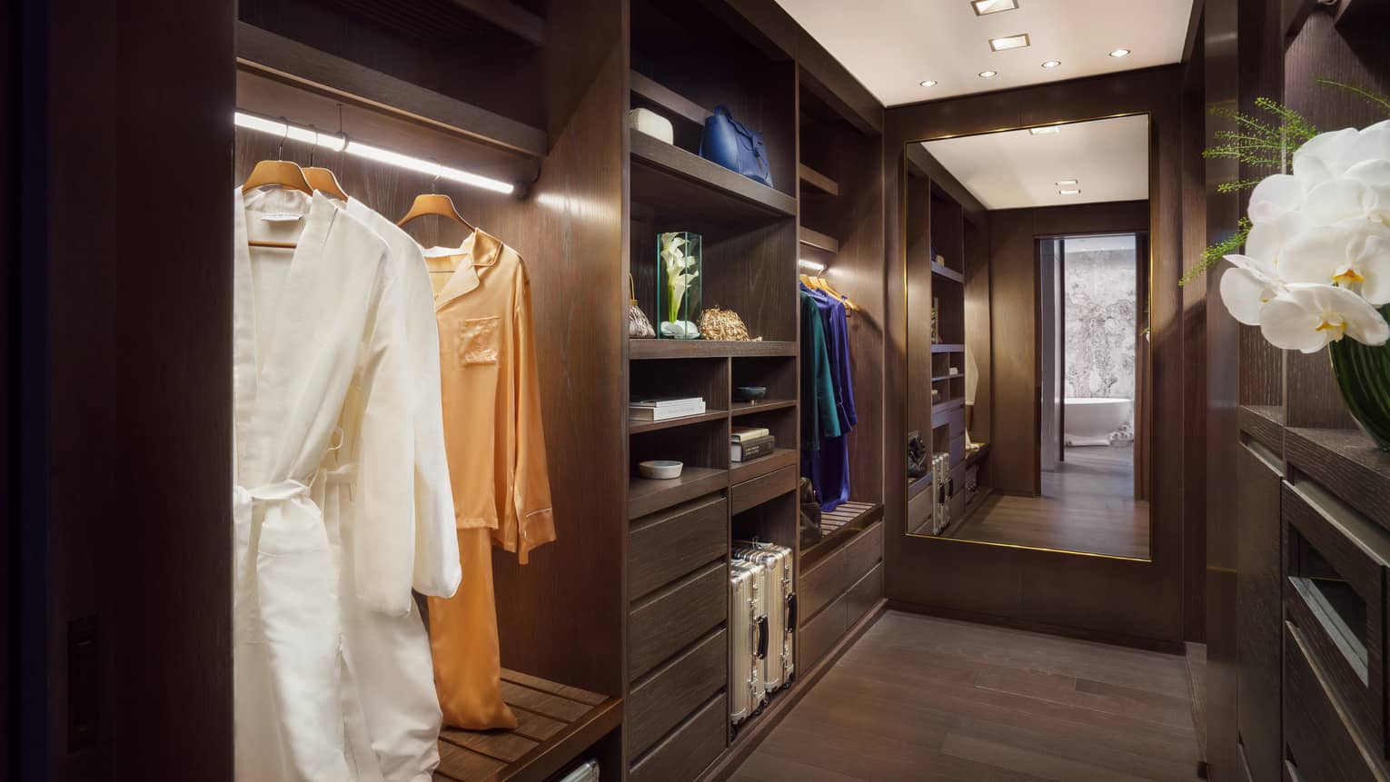 Large walk-in closet with built-in shelving, dark wood floors, floor length mirror