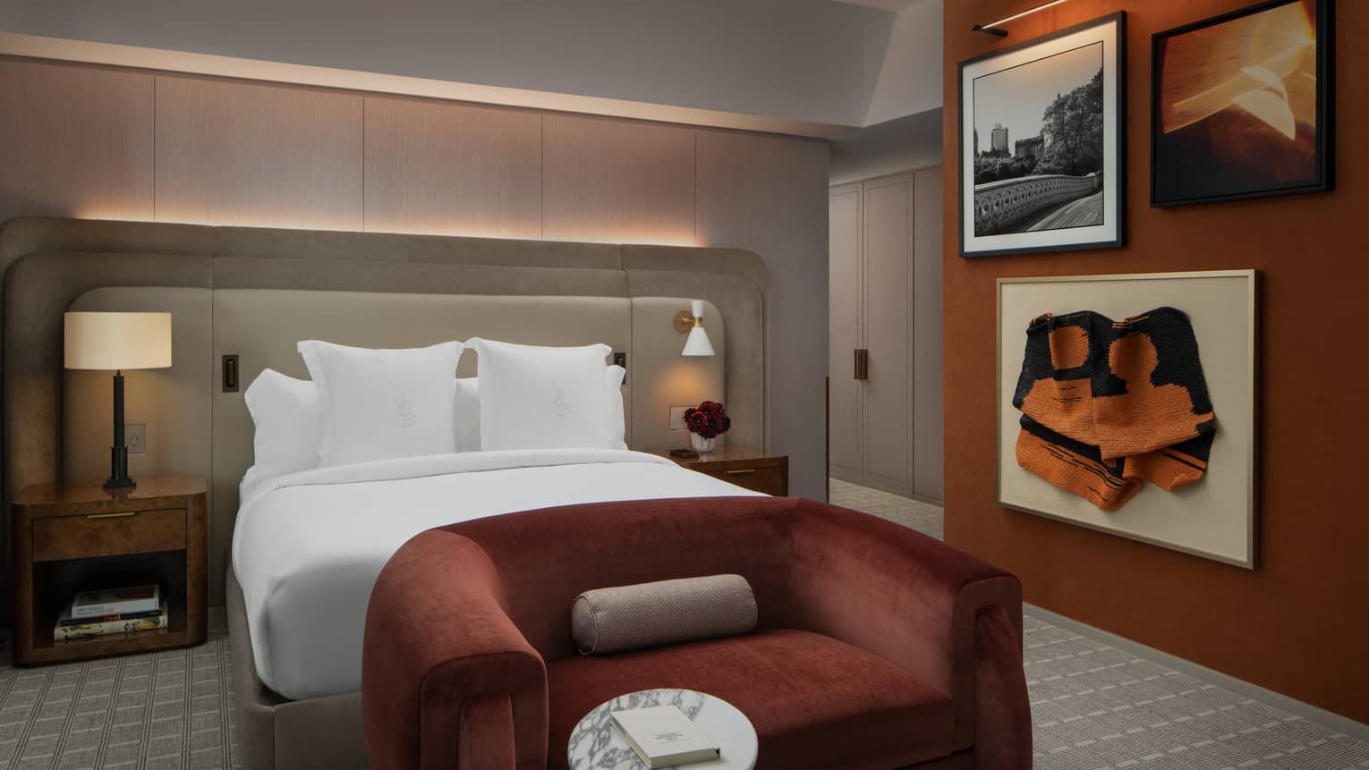 Hotel bedroom with king bed, deep red velvet love seat and three pieces of artwork on the wall