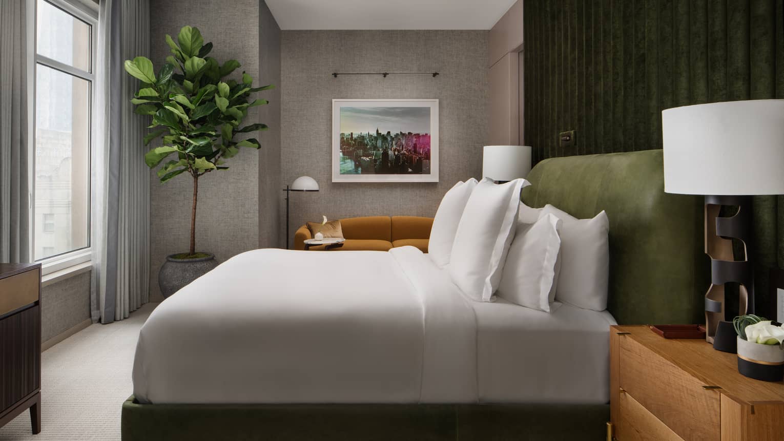 Hotel room with king bed, forest-green accent wall, tree and city-view window