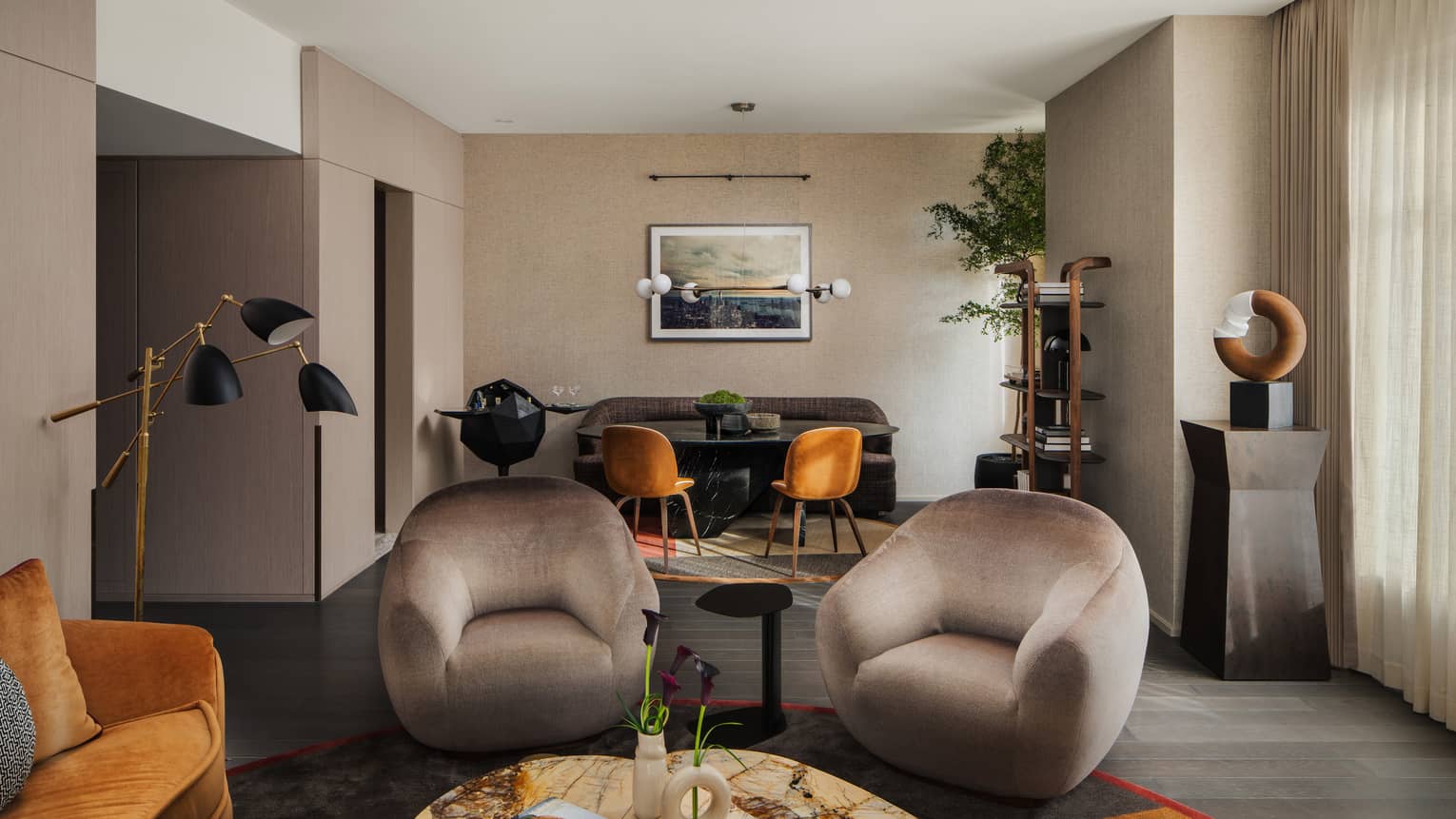 Luxury living and dining area with beige armchairs, marble table, dining set with sofa, wall artwork, and black bar cart