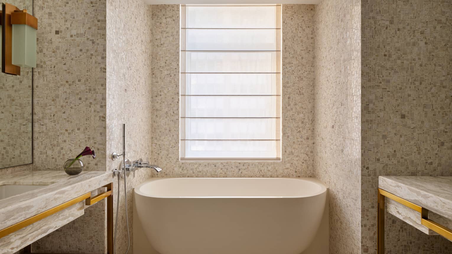 Modern hotel room bathroom featuring a standalone oval tub next to a window