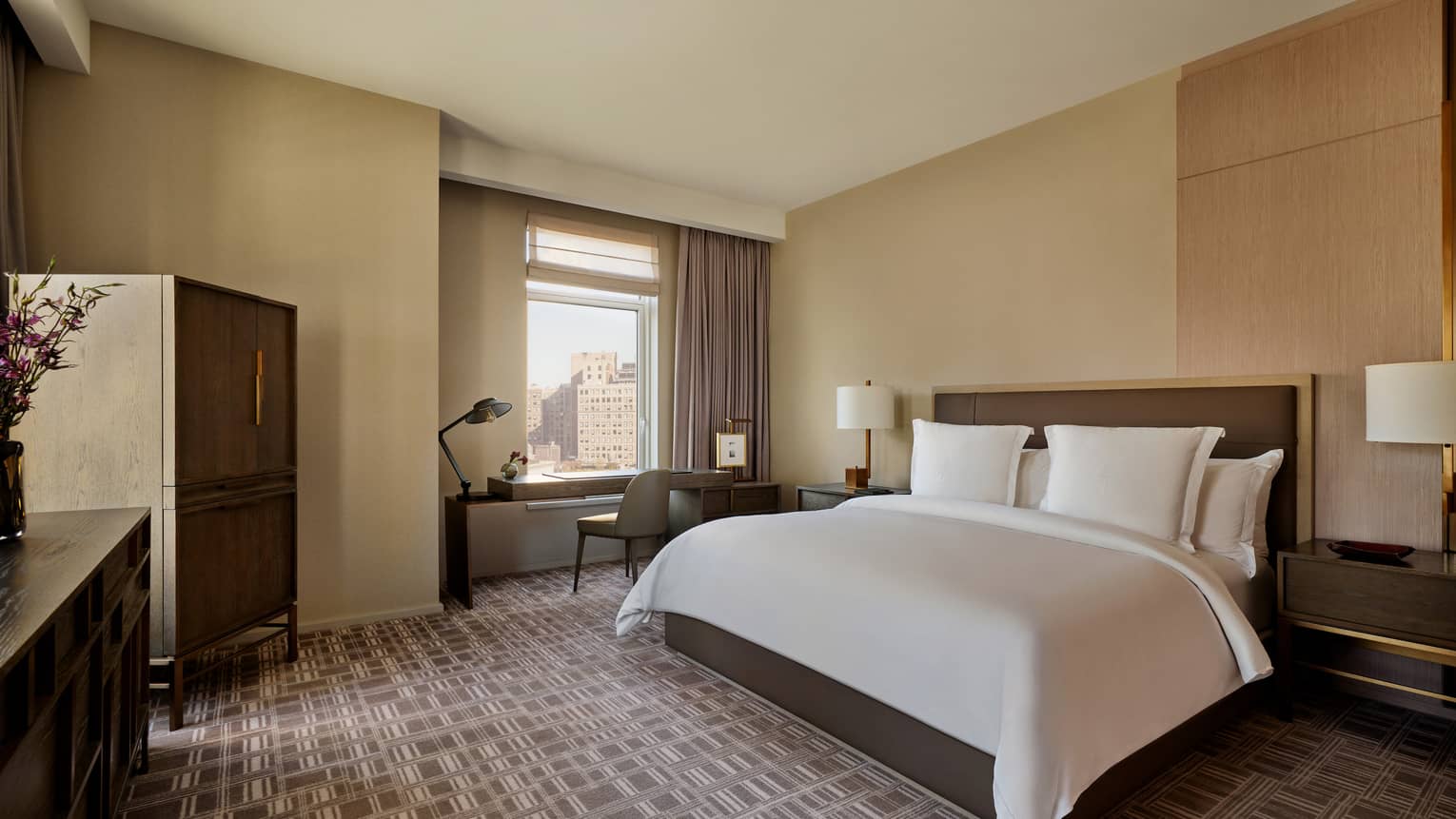 Modern hotel room with king bed, tile-looking carpet, and desk by the window