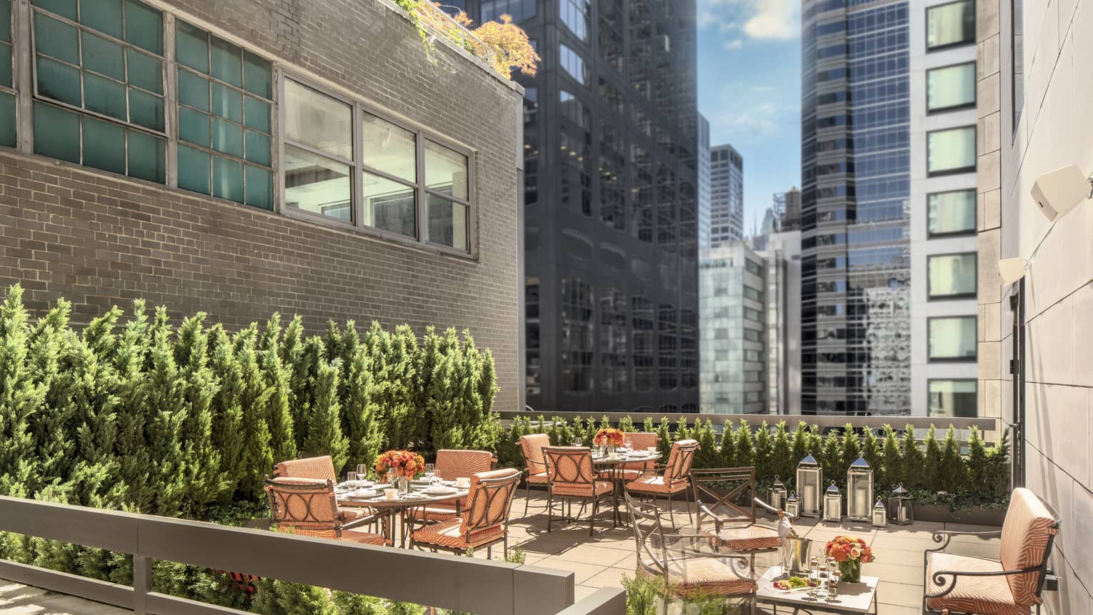 11th Floor Terrace Boardroom, surrounded by green topiaries, with square iron and glass tables with orange cushions on chairs at Four Seasons Hotel New York