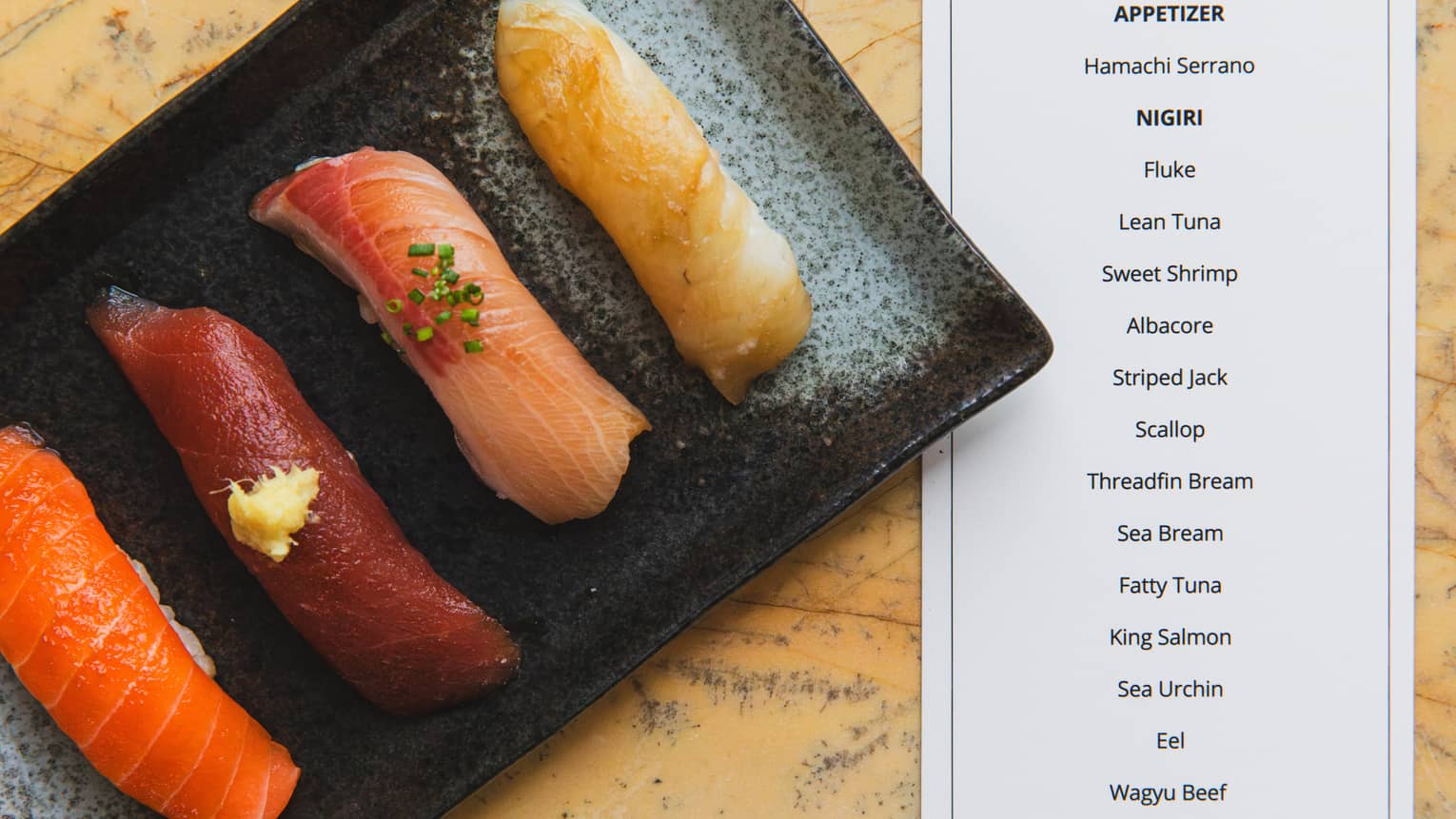 Sashimi on a black tray next to a 17-course menu