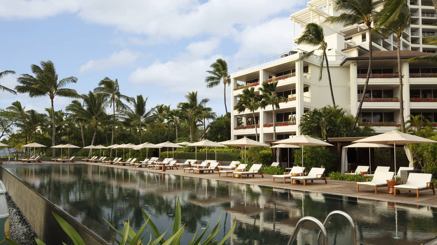 Exterior building and outdoor pool lined with white lounge chairs at tropical Resort