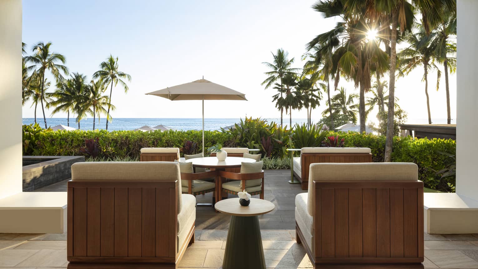 Contemporary private outdoor terrace of a resort suite, with dining table and lounge chairs facing palm trees and ocean