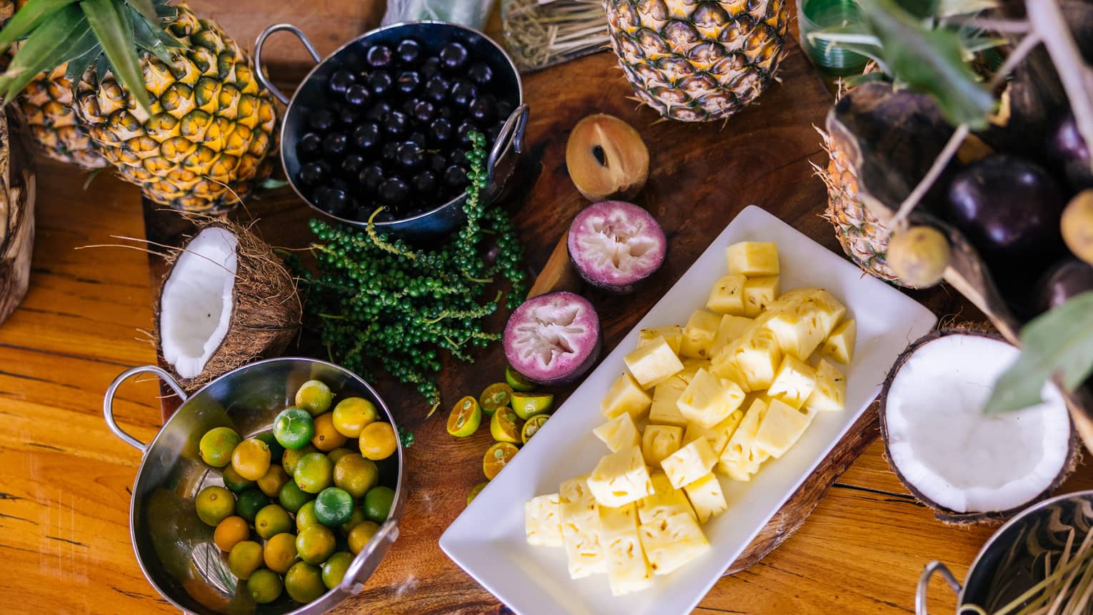 Table set with plate of cubed pineapple, bowl of berries, a halved coconut and other fruits