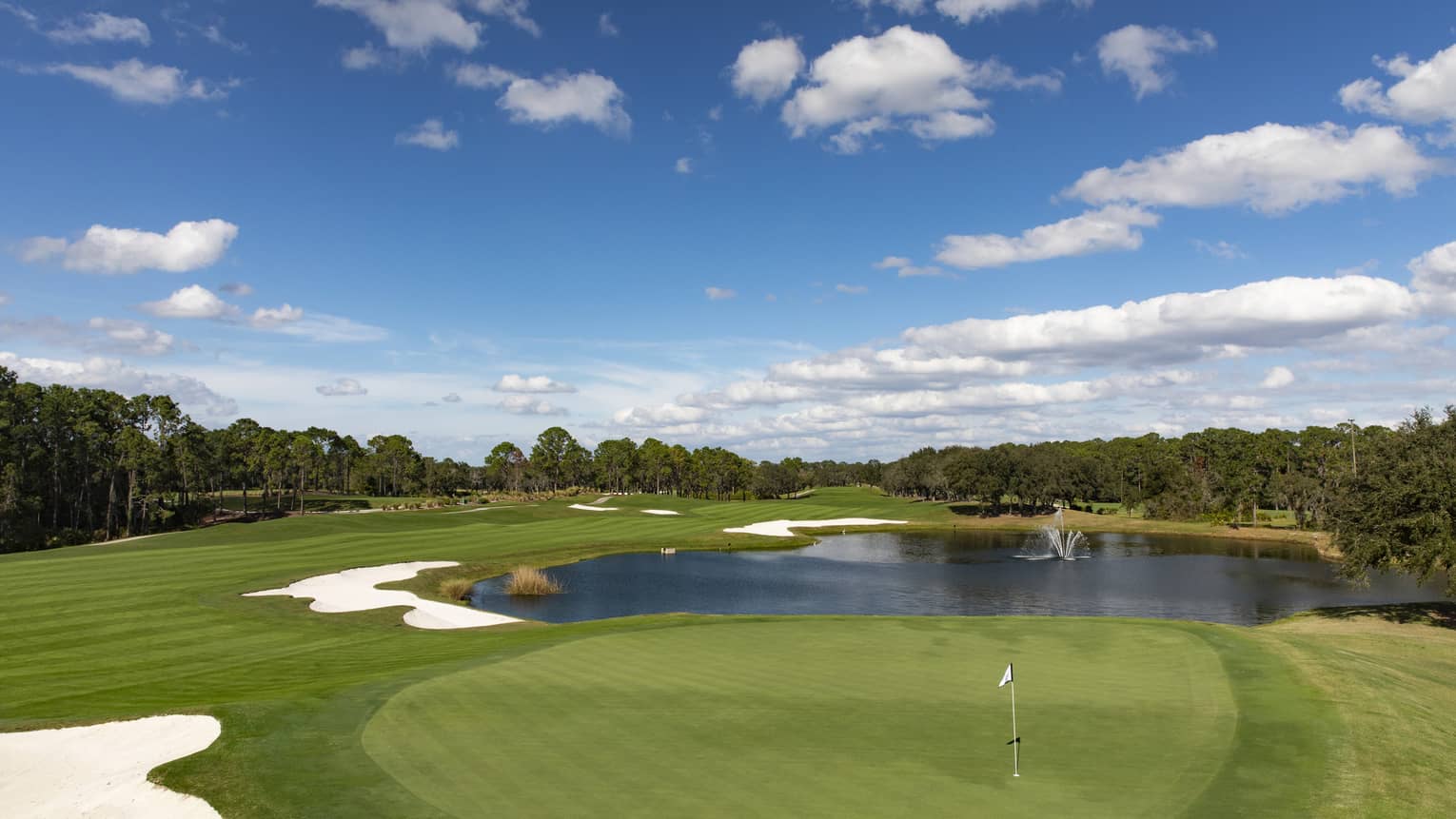 View across golf course green, small pond under blue sky 
