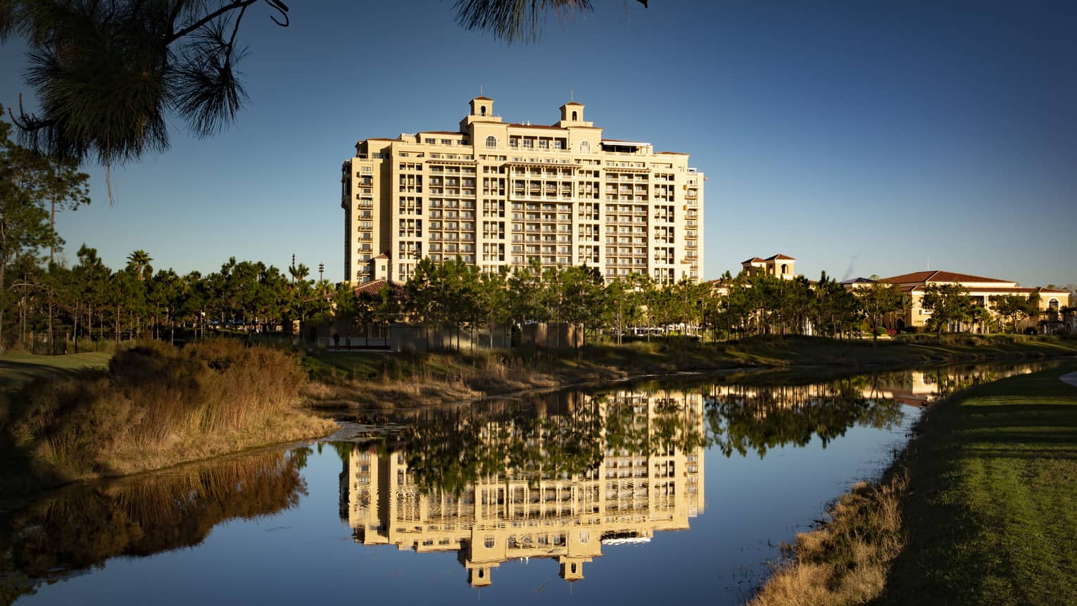 View across water, trees to Four Seasons Resort Orlando at Walt Disney World® Resort building exterior against blue sky