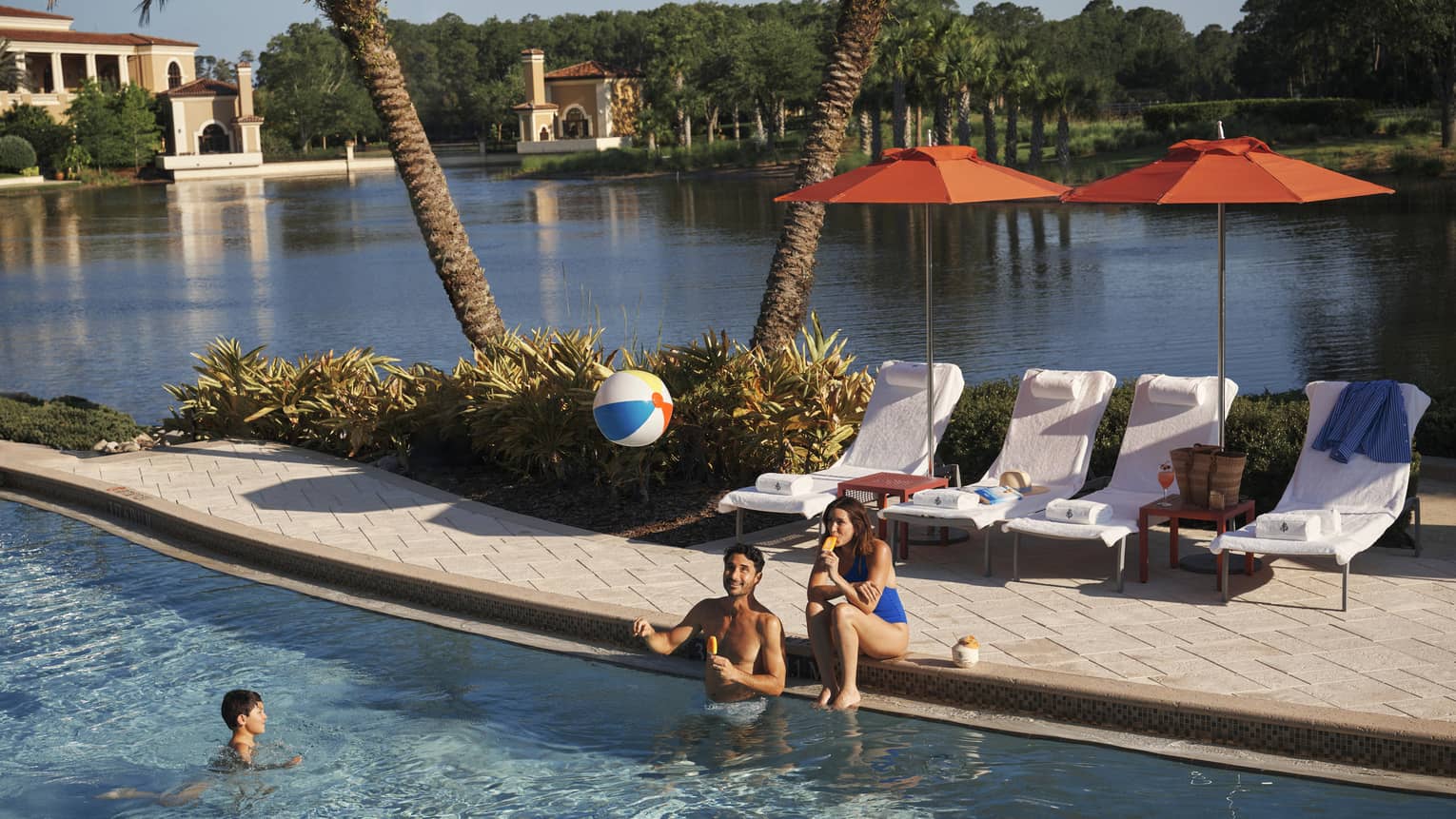 Two adults play with kid and a beach bar in the family pool at luxury resort