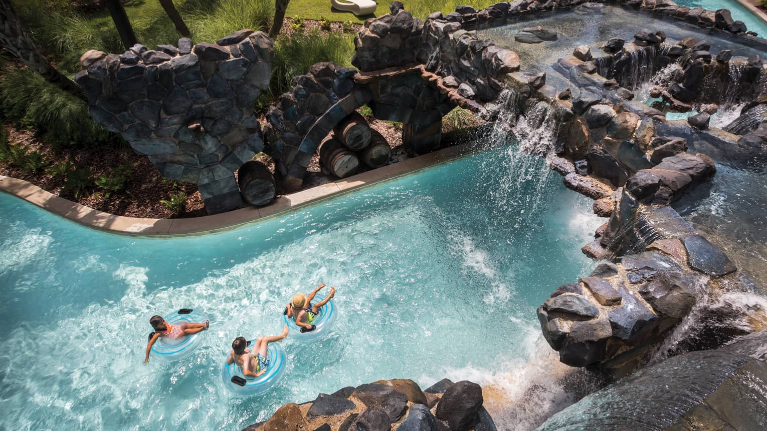 A bird's-eye view of three people floating in inner tubes down a rock-lined lazy river pool at four seasons resort orlando at Walt Disney World