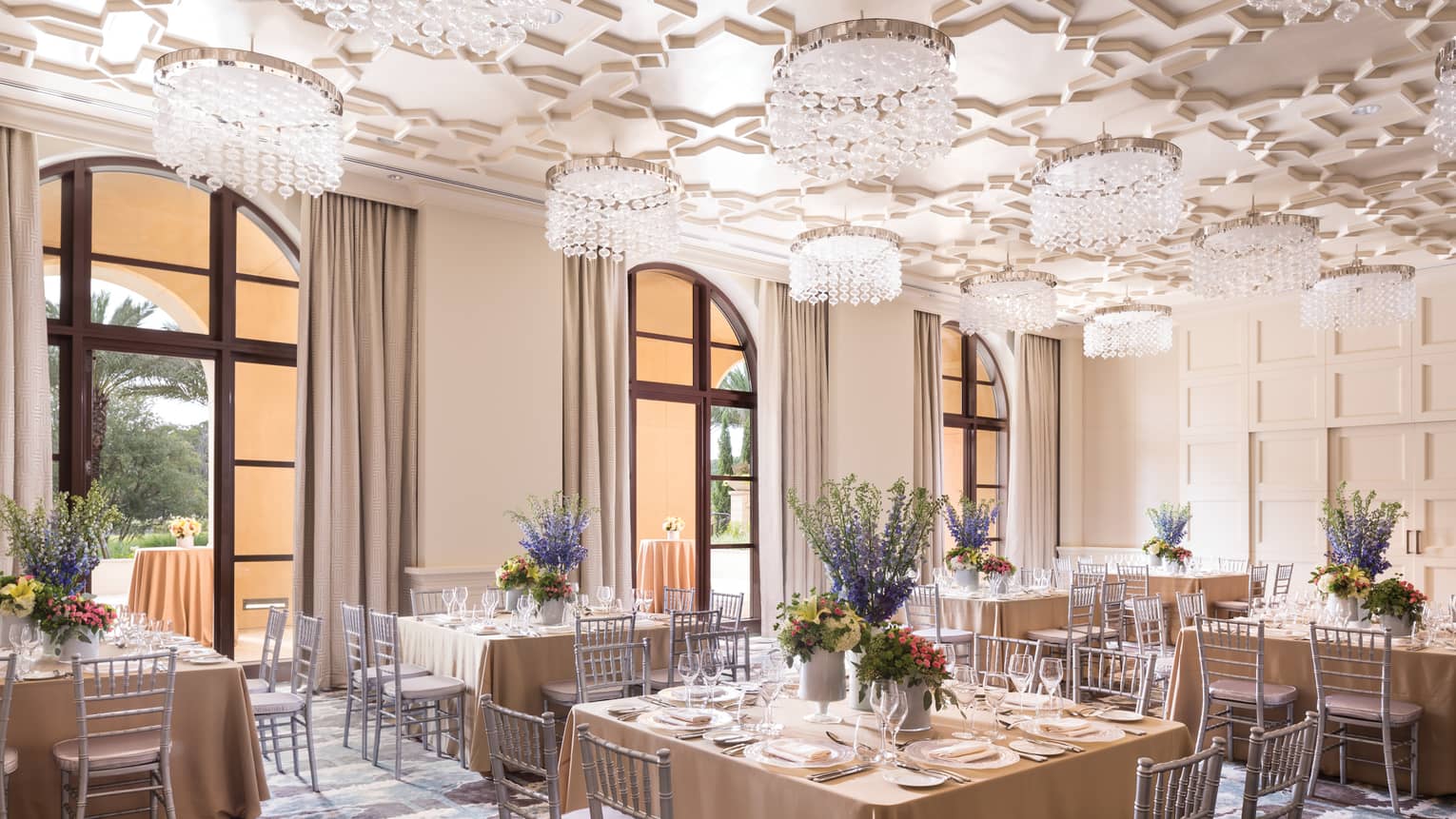 Square banquet dining tables under geometric ceiling with crystal chandeliers 