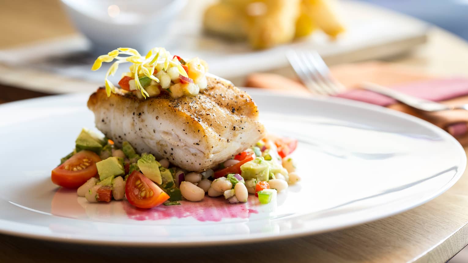 Thick, roasted white fish filet on bed of white beans and vegetables, garnished with fresh salsa