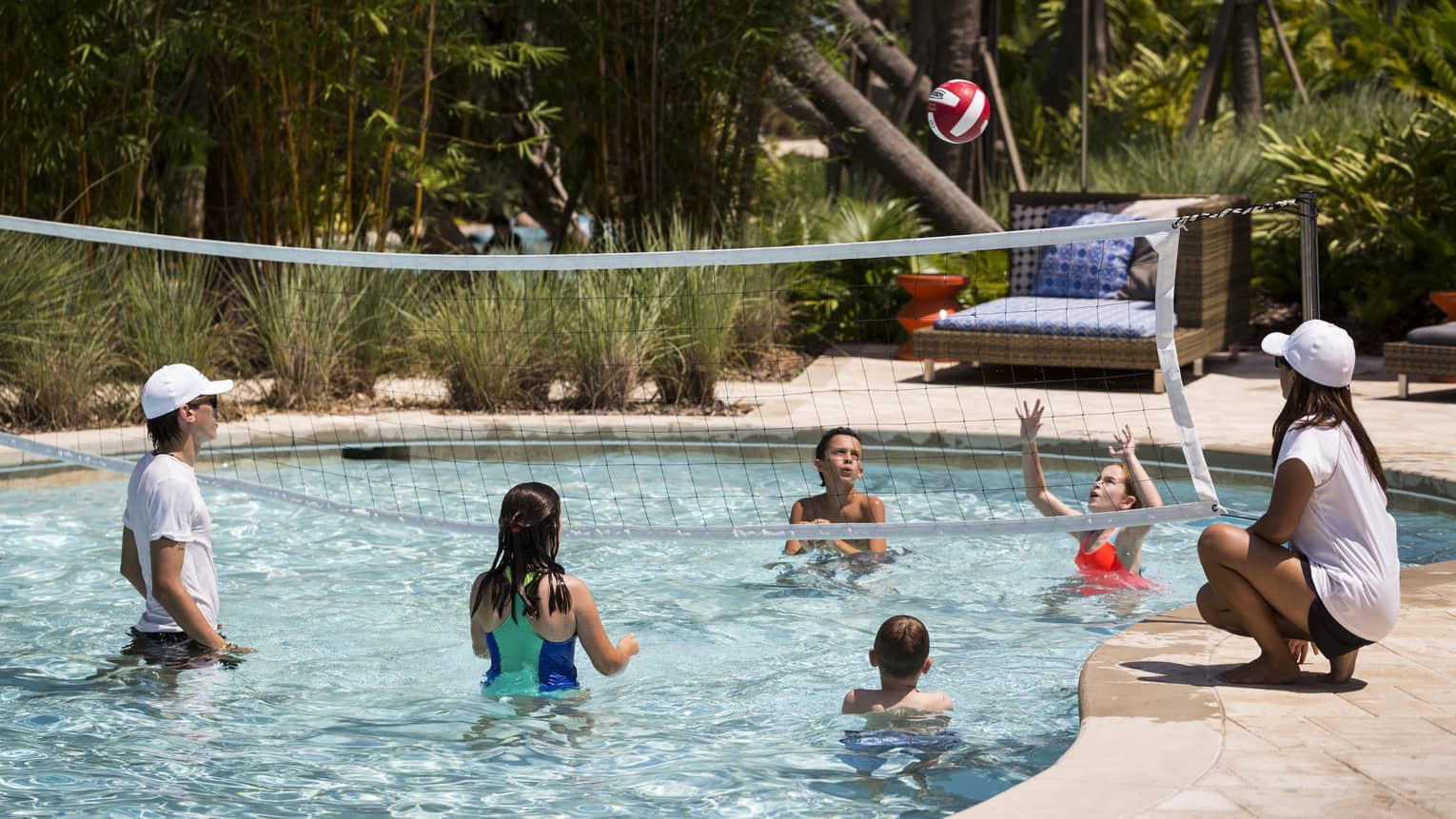 Kids play volleyball in small outdoor swimming pool with net