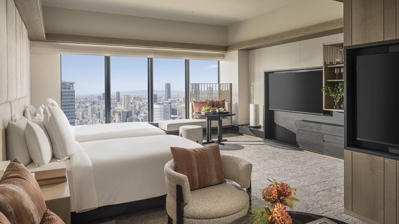 Hotel suite with two beds and TV, wall of windows, and a sitting area with a second TV