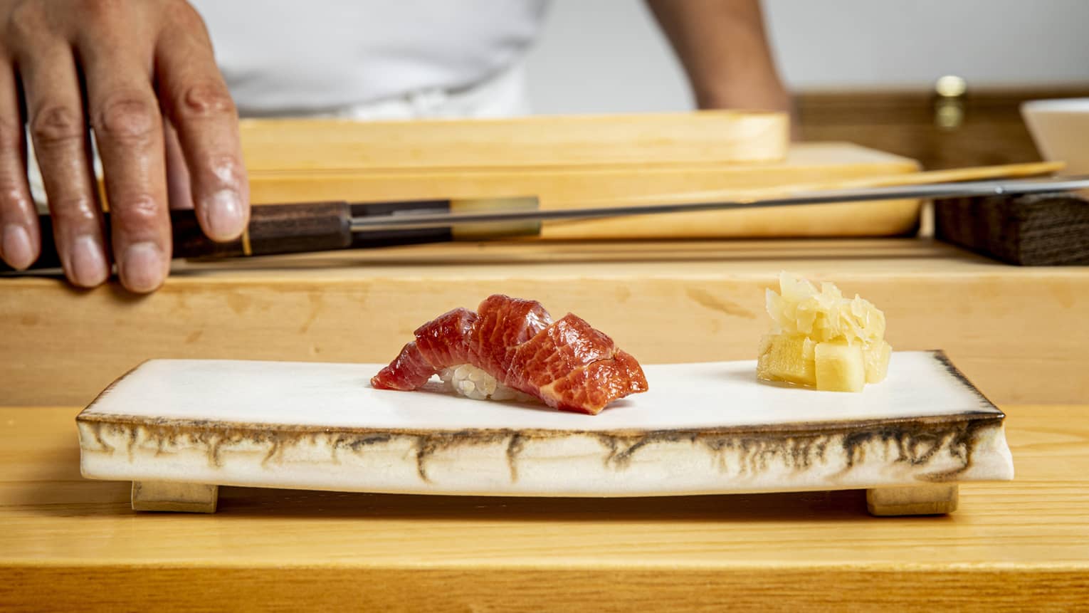 Edomae sushi on a modern stone plate, with a chef and chef's knife in the background