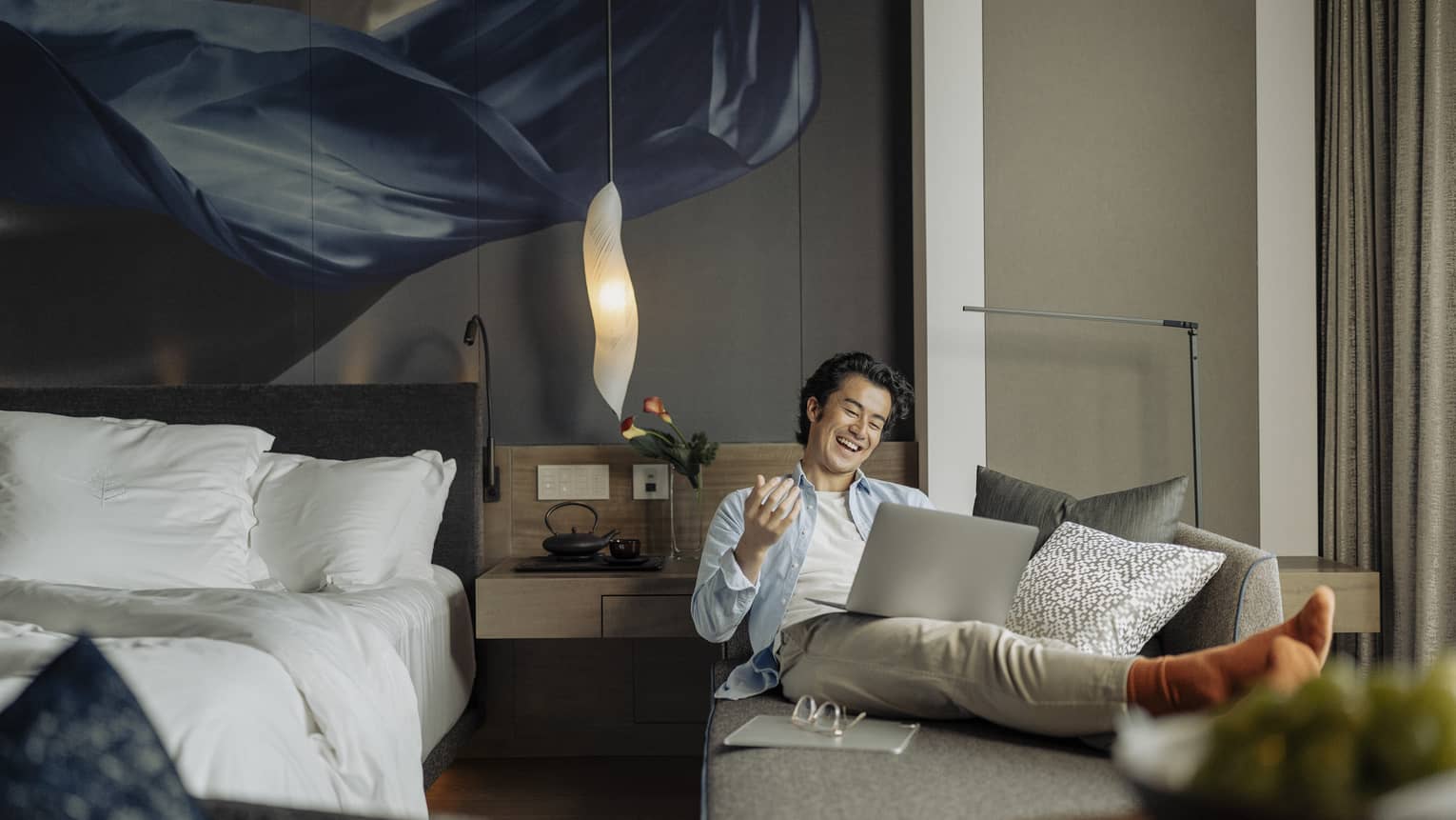 Laughing man lounges on sofa with laptop in his guest room