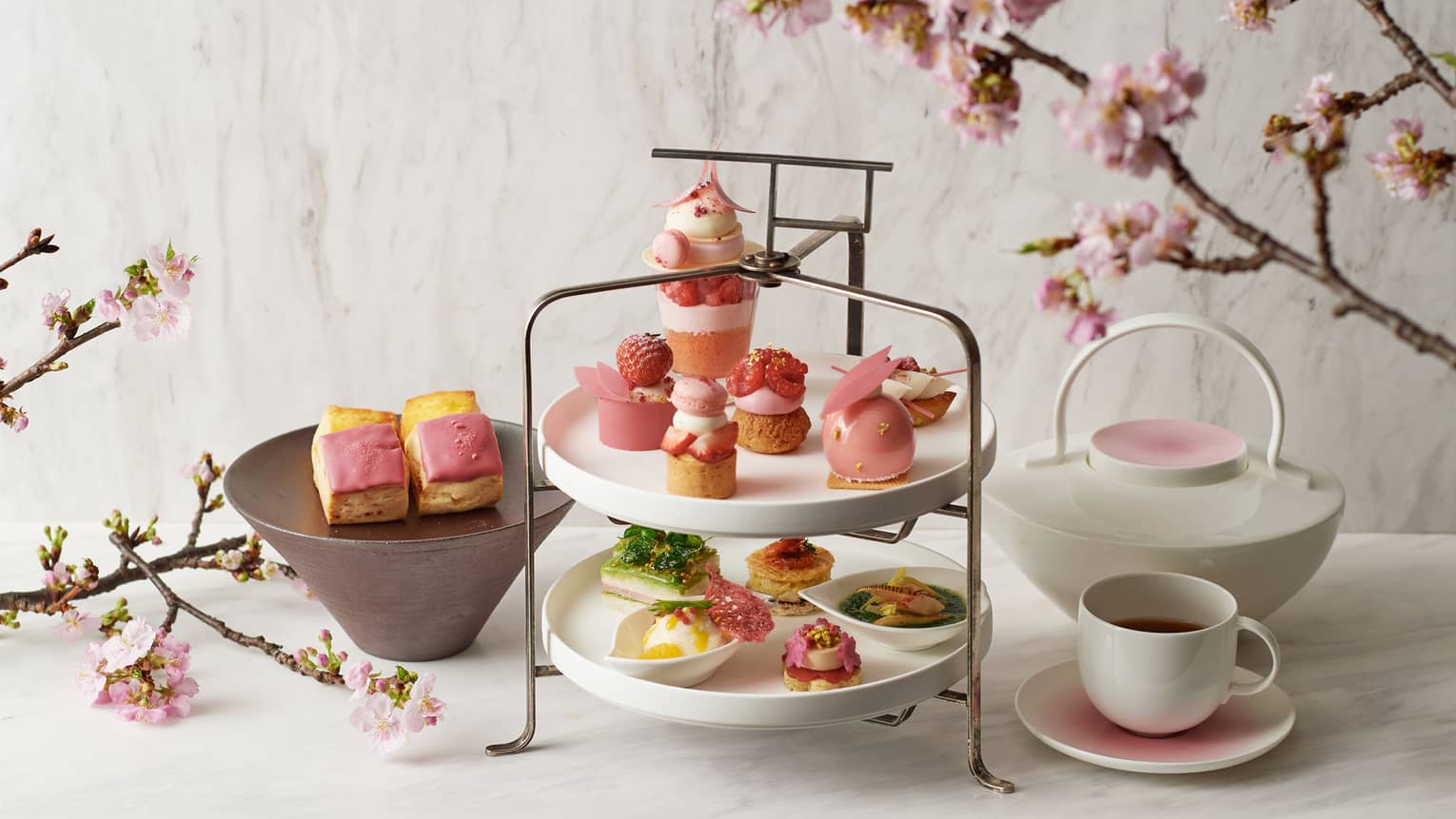 Sakura Afternoon Tea spread with pink sweets, pot of tea and mug, cherry blossom branches