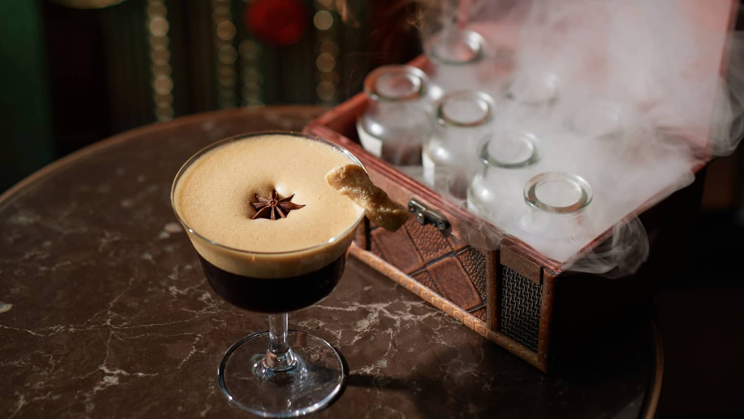 Geisha Martini in stemmed glass with espresso foam and star anise garnish, basket of steaming empty milk bottles