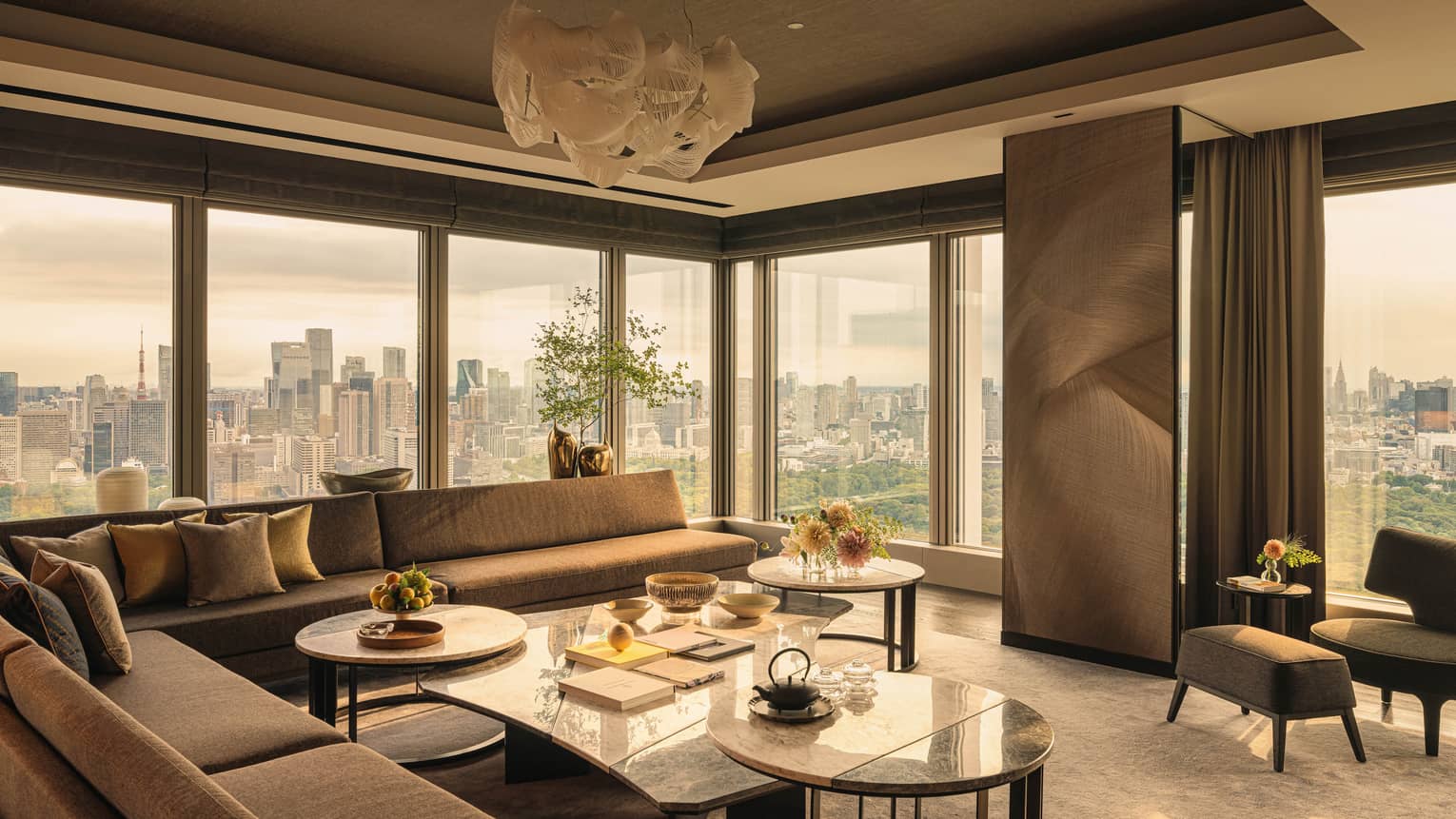 Luxury hotel suite featuring sectional sofa, a cluster of coffee tables, modern lighting fixture and city views