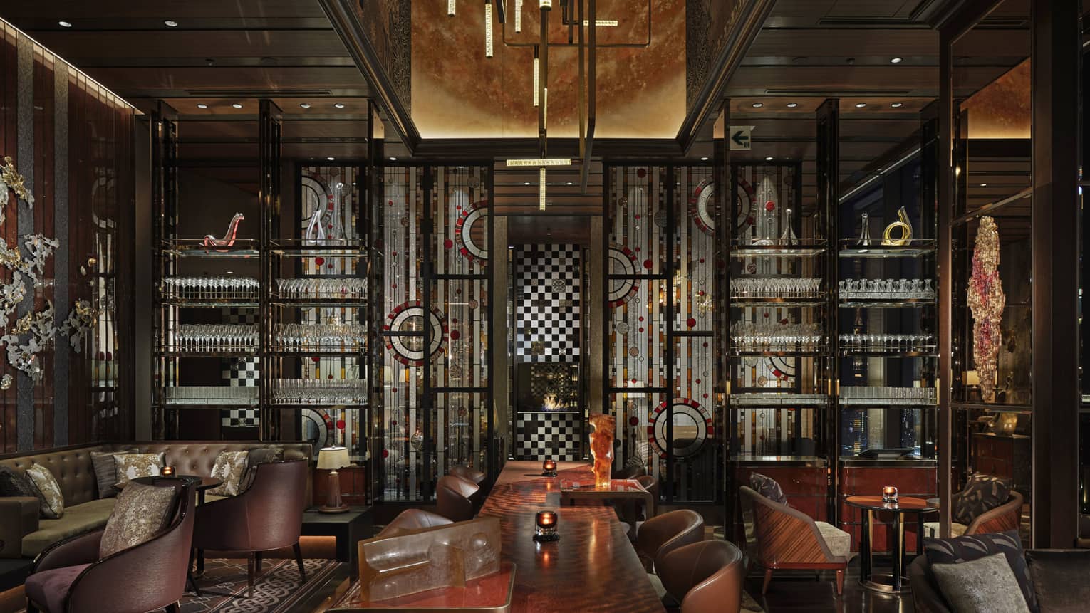 Lounge area with lounge chairs and ergonomic table in the center, shelves of cocktail glasses, lowlighting, muted tones
