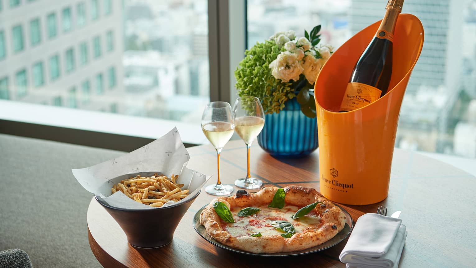 Champagne, pizza, fries and flowers on table in hotel guest room overlooking Tokyo