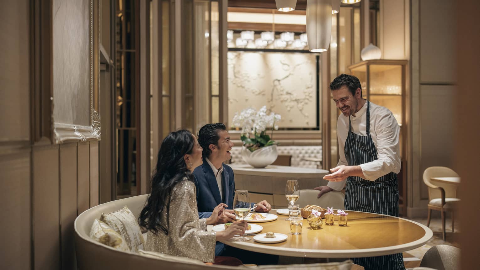 Couple dines at circular table at est, sommelier presenting them with a bottle of wine