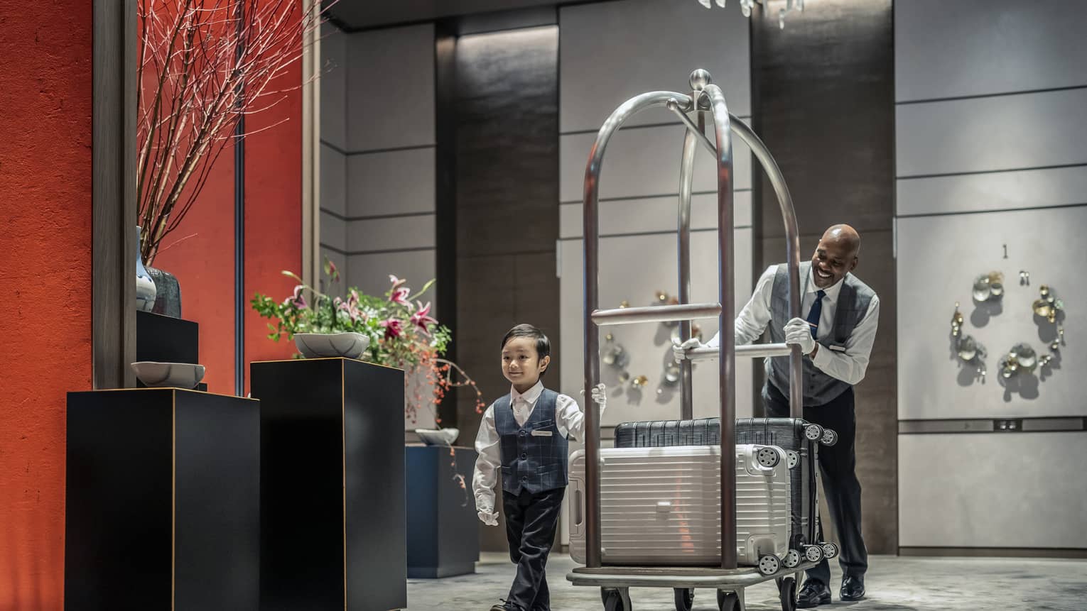 Little boy helps bellman pull luggage cart through lobby