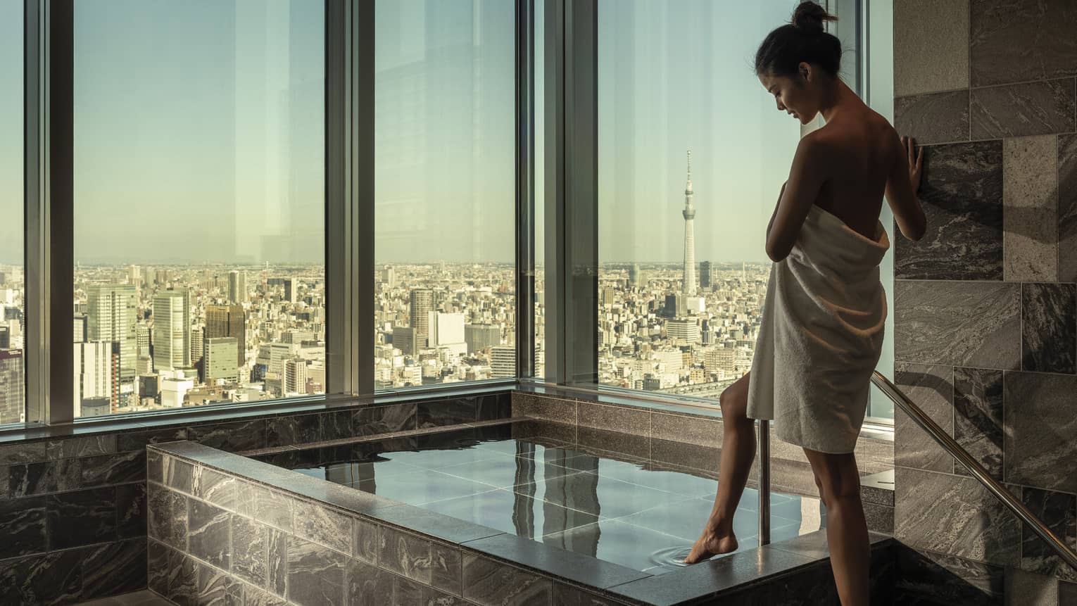 Woman wrapped in white towel dips her toe into the ofuro bath