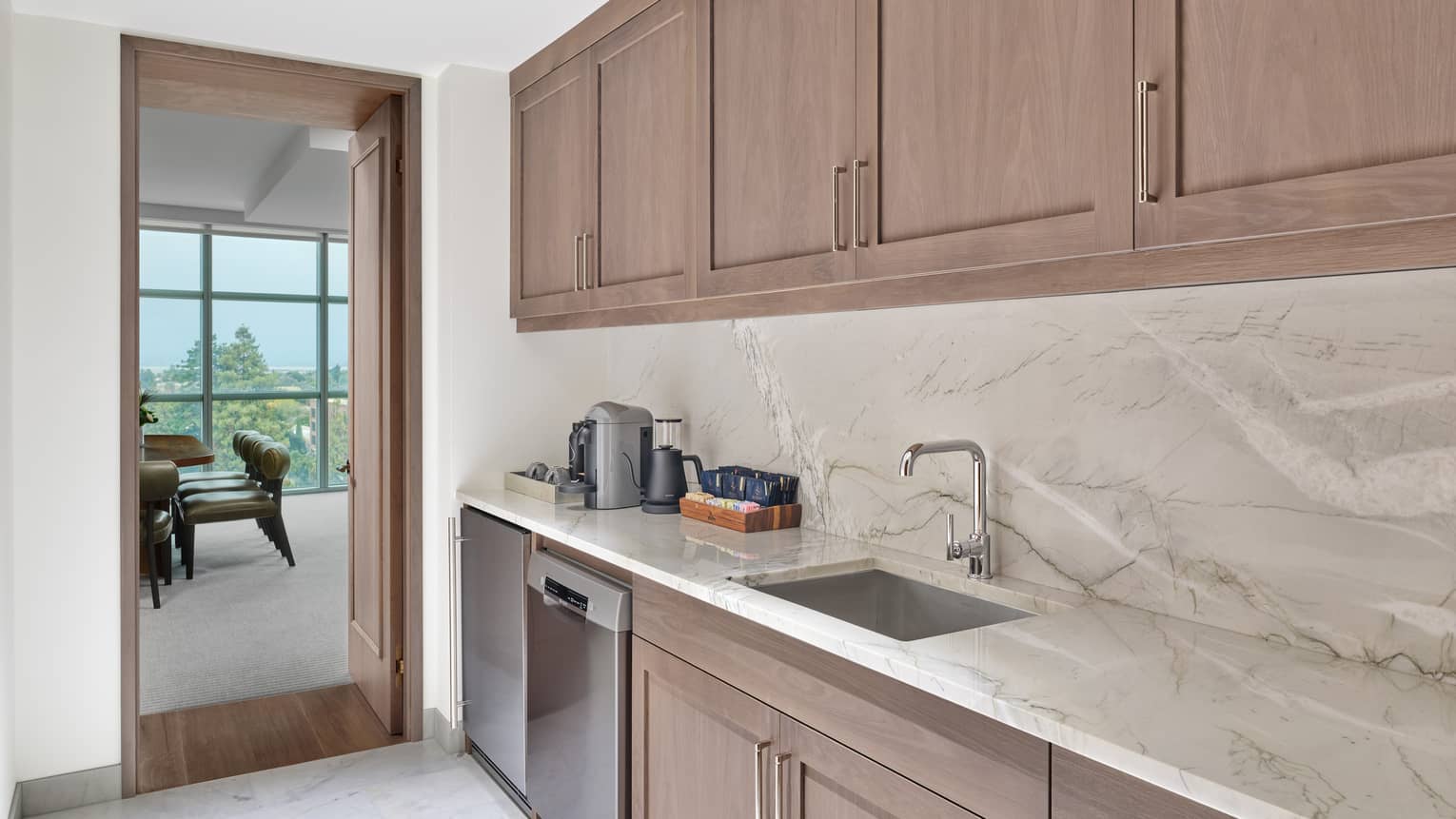 Kitchen with marble countertops and backsplash, leading into dining room of hotel suite