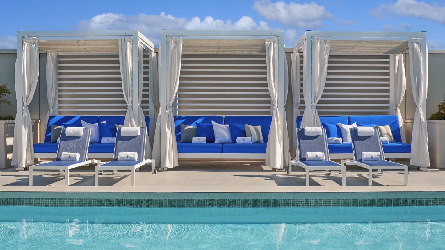 Three blue couches in cabanas by the pool.