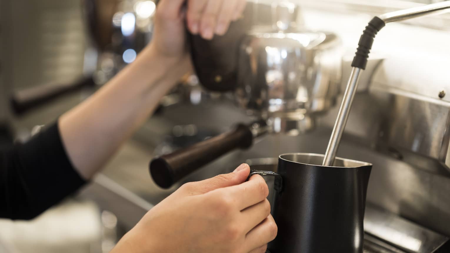 Close-up of hands with milk steamer at espresso machine