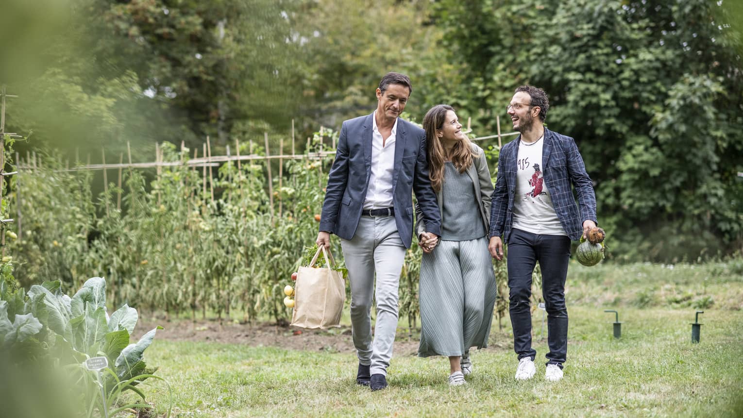 Three people holding bags with fresh produce walk away from vegetable garden