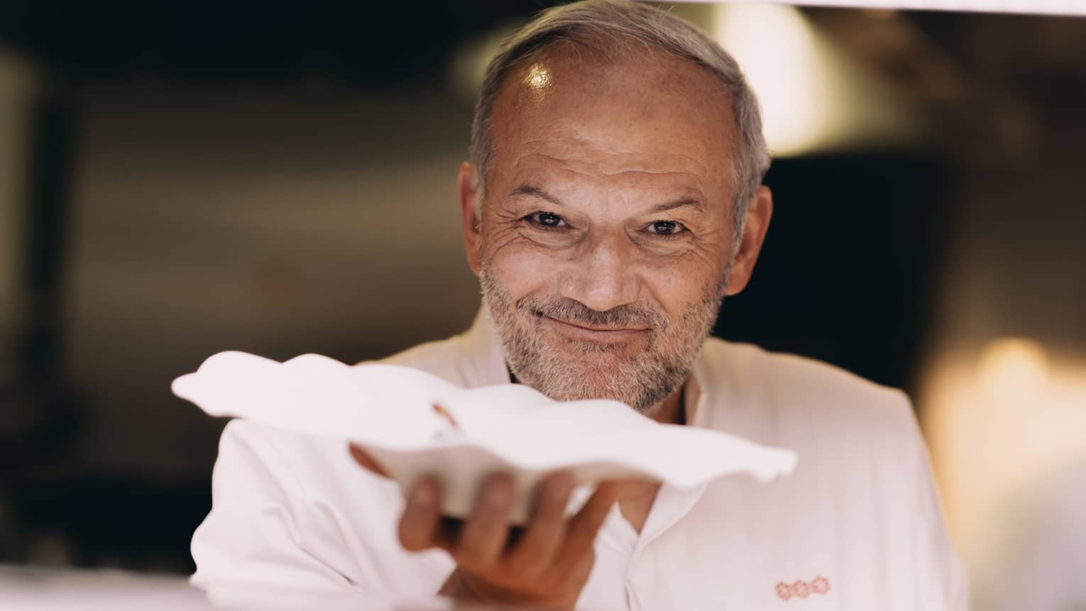 Chef Christian Le Squer smiling, handing out white scalloped dish