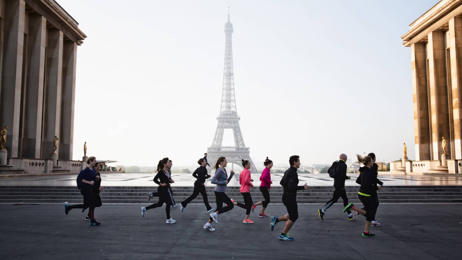 Group of runners jogs past Eiffel Tower on brick path