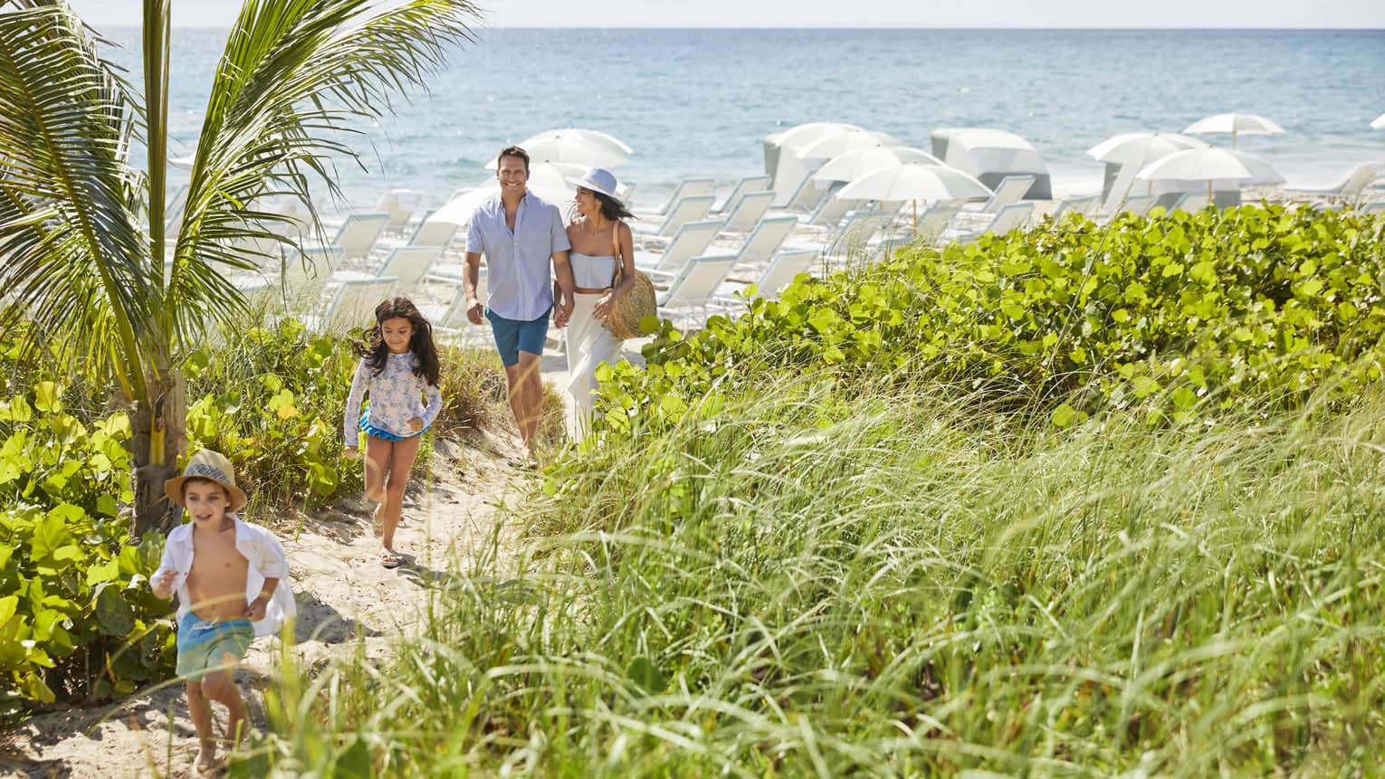 A family departs from the beach down a sandy path, smiles on their faces