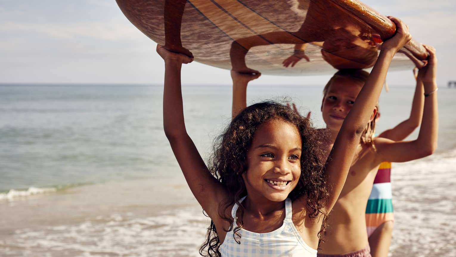Three young children carrying a surfboard.