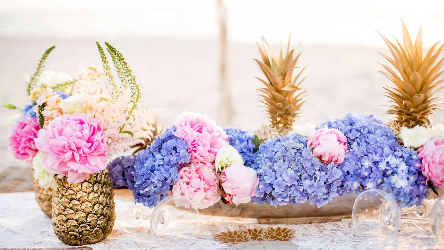 Vibrant pink and purple flowers are displayed around pineapples