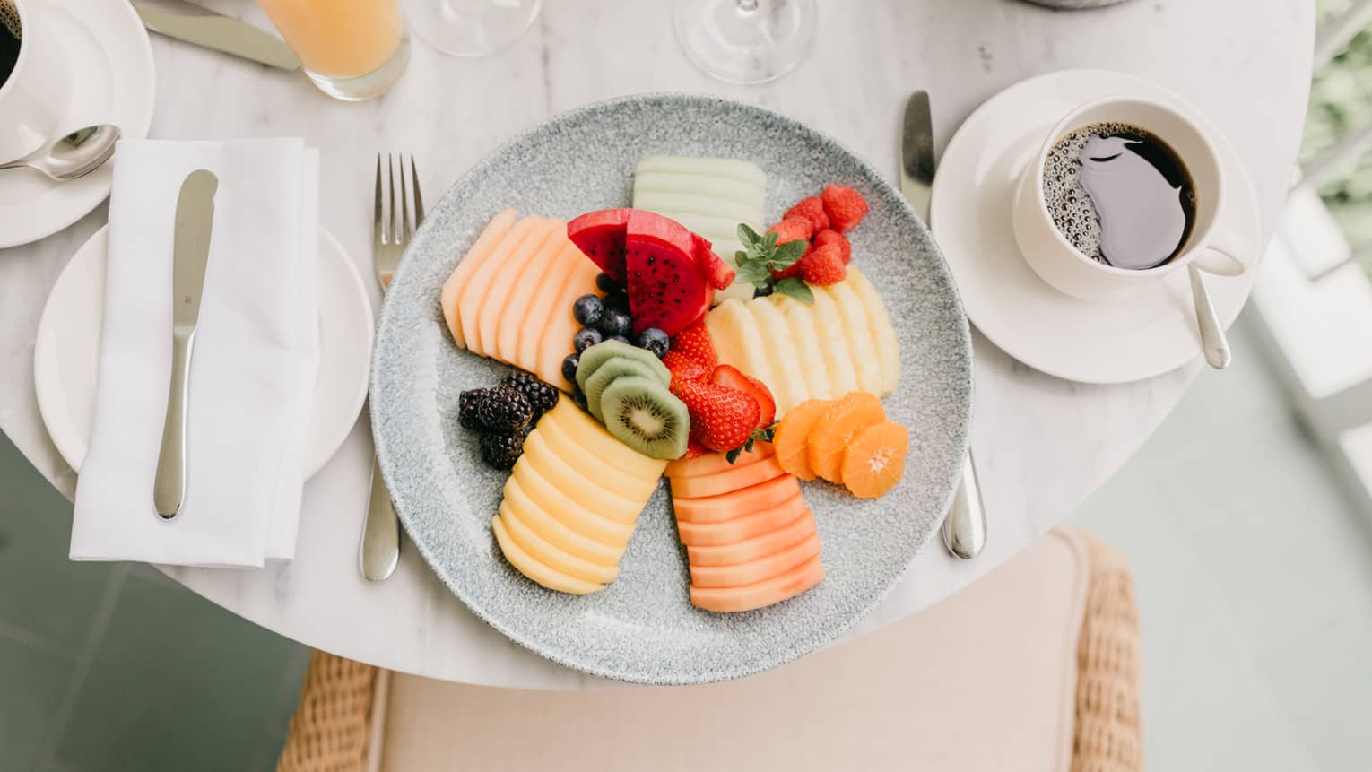 Plate of assorted sliced fruits and whole berries, place setting, coffee