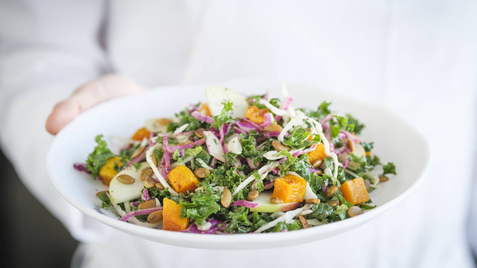A chef holding a white plate with a salad on it.