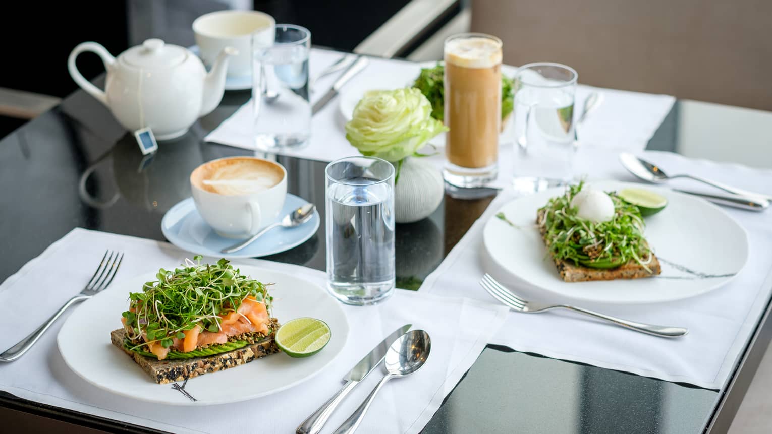 Three plates of toast with avocado and salmon on them, along with cups of coffee and water.