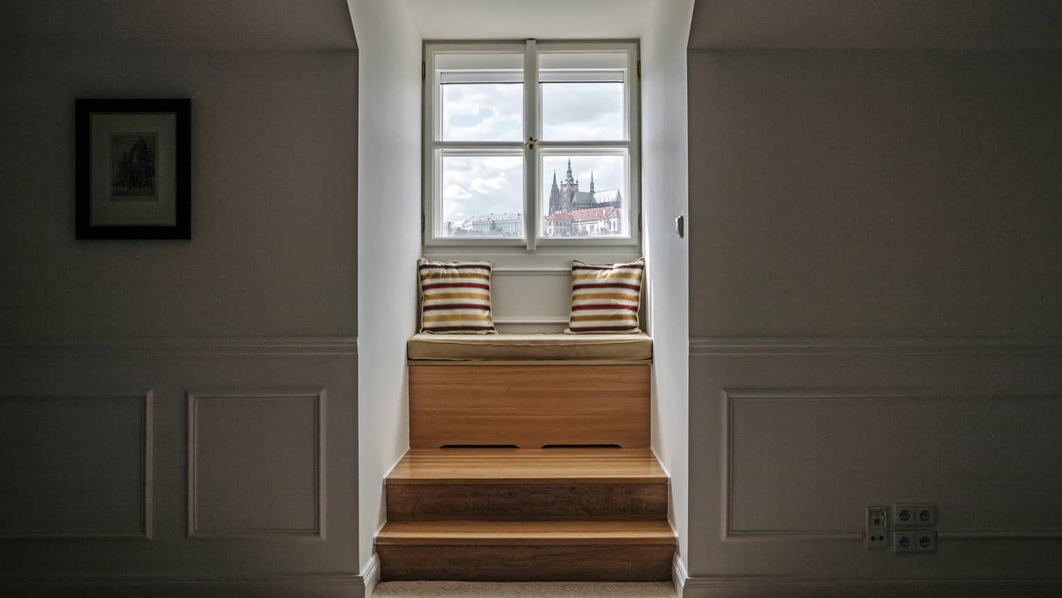 Wooden steps up to window seat dressed with two striped pillows by window with castle view