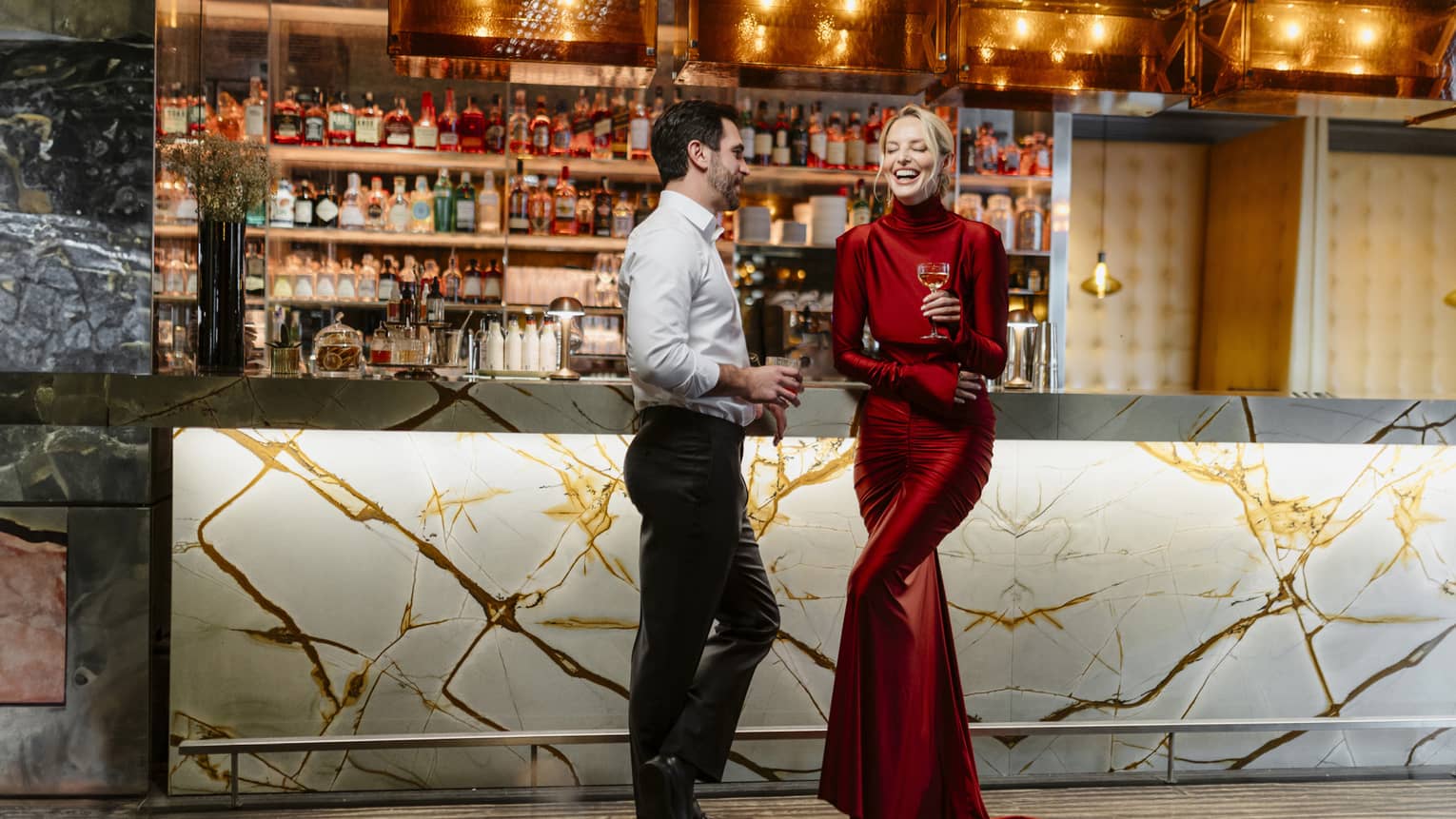 Couple standing, laughing in front of a dimly lit stocked bar