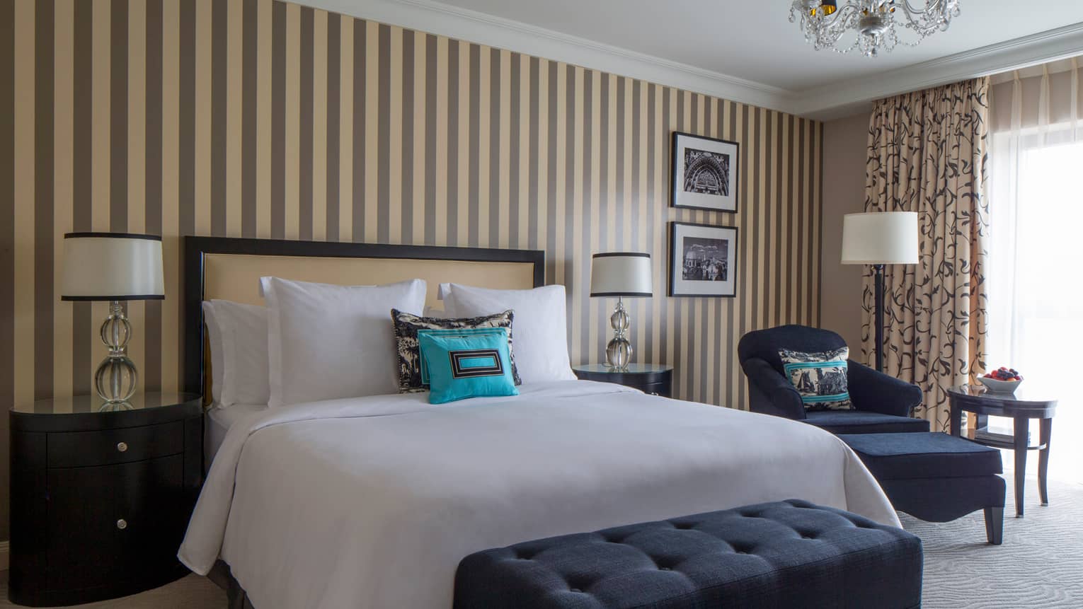 Modern Room bed with white linens, small turquoise pillow, against wall with grey-and-cream coloured striped wallpaper