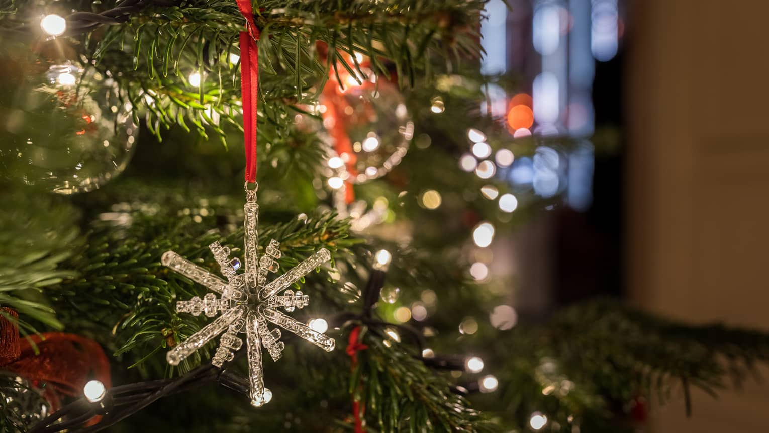 Close-up of a crystal snowflake ornament hanging on a Christmas tree with festive lights in the background