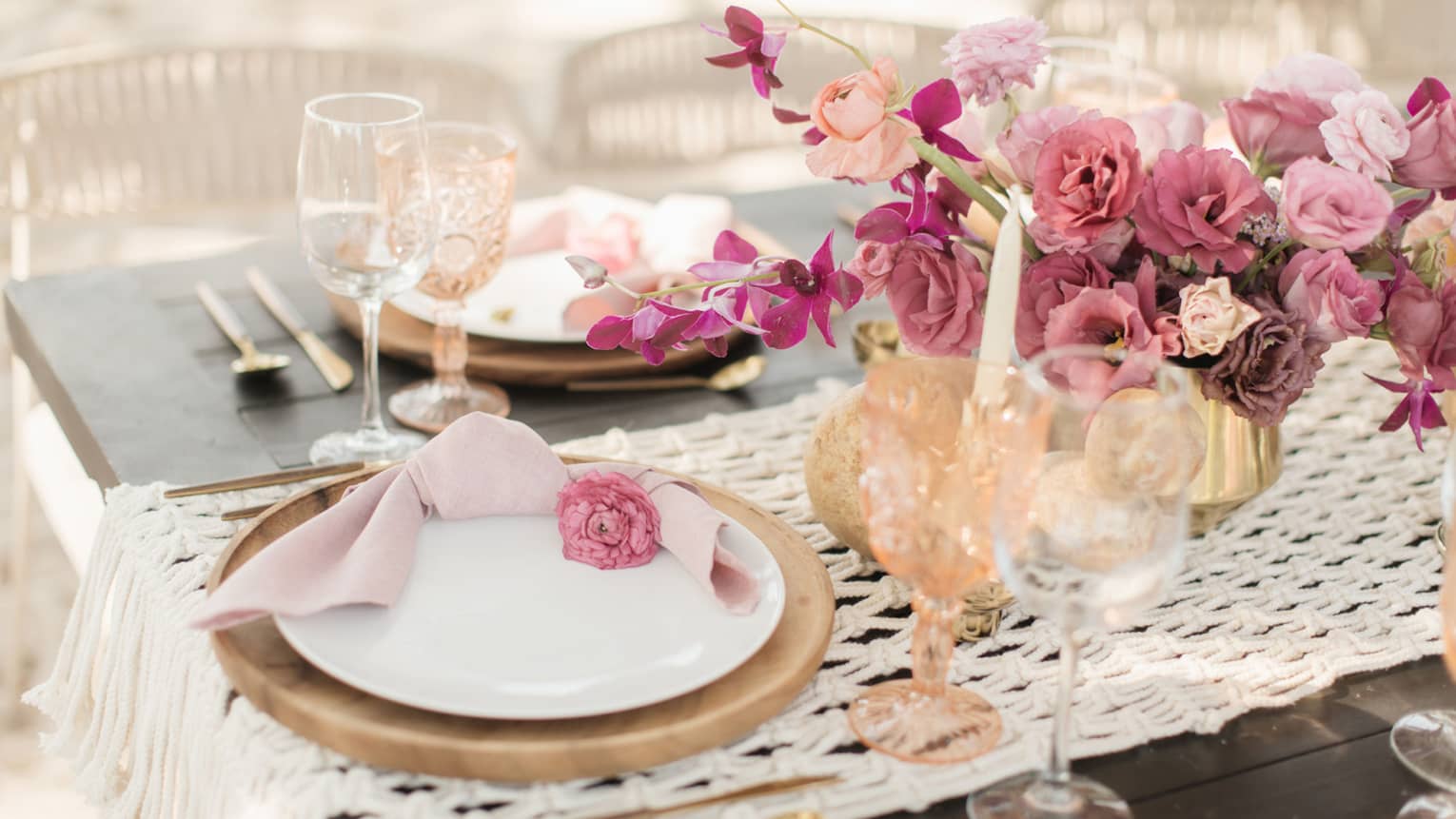 A table with wedding decorations of white plates, wine glasses, and light red and pink roses.