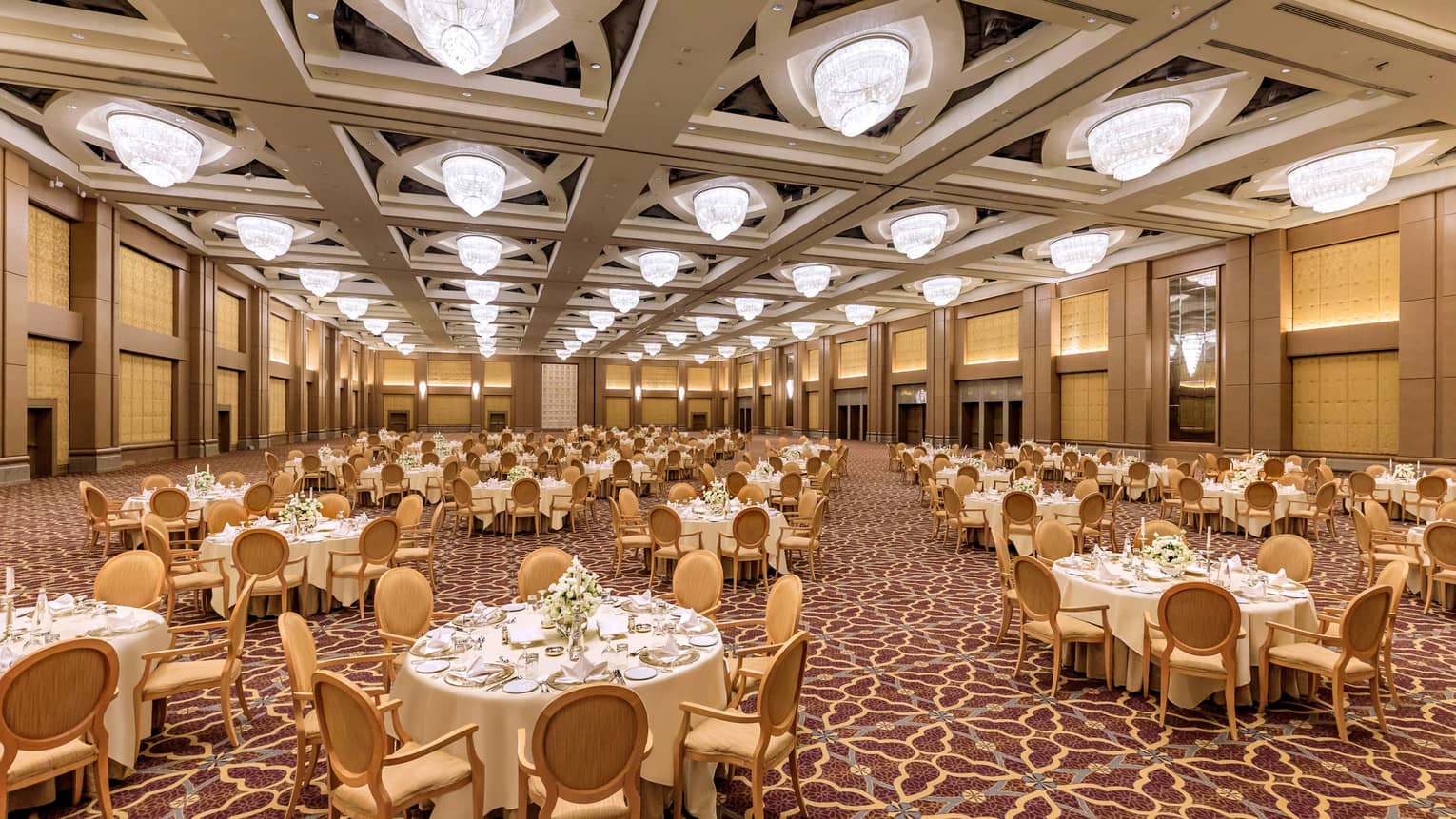 Grand ballroom with banquet tables set for event. Patterned carpeting and ceiling with squares of lights.