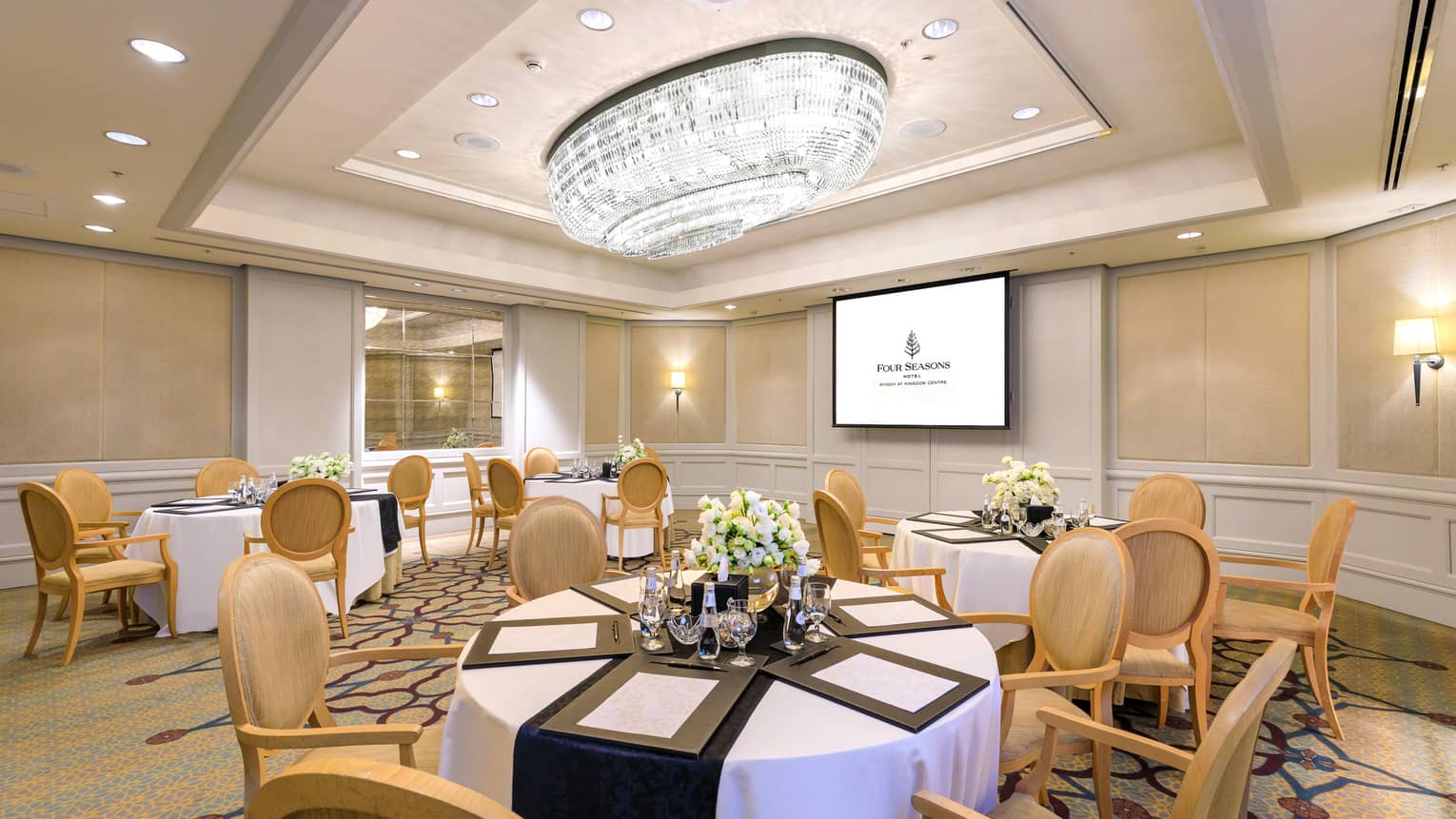 Elegant hotel meeting room with six banquet tables, presentation screen and crystal chandelier